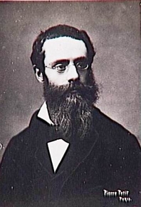 Photographie noir et blanc montrant un homme tourné de trois-quart, portant une barbe et des lunettes.