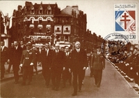 Carte postale noir et blanc montrant un groupe d'hommes marchant dans une rue.