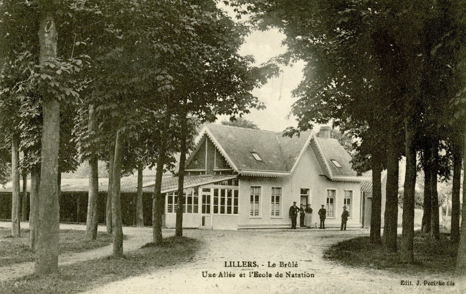 Carte postale noir et blanc montrant une bâtisse au détour d’un chemin bordé d’arbres.