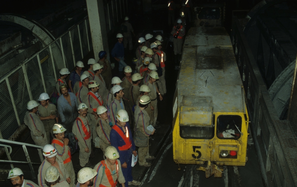 Photographie couleur montrant un groupe d'ouvriers devant un wagonnet jaune.