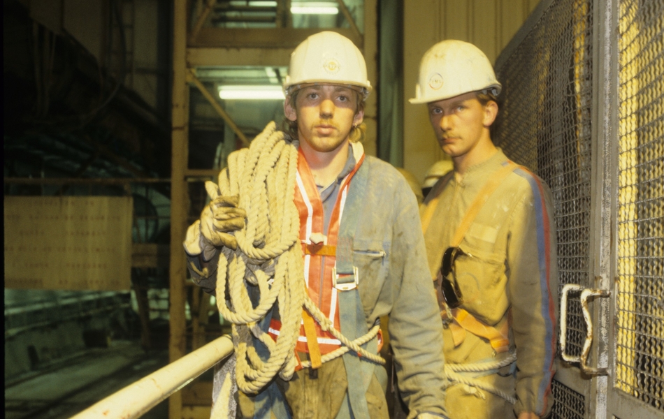Photographie couleur montrant deux ouvriers vêtus d'une tenue de chantier et portant des cordes et un casque de chantier blanc.