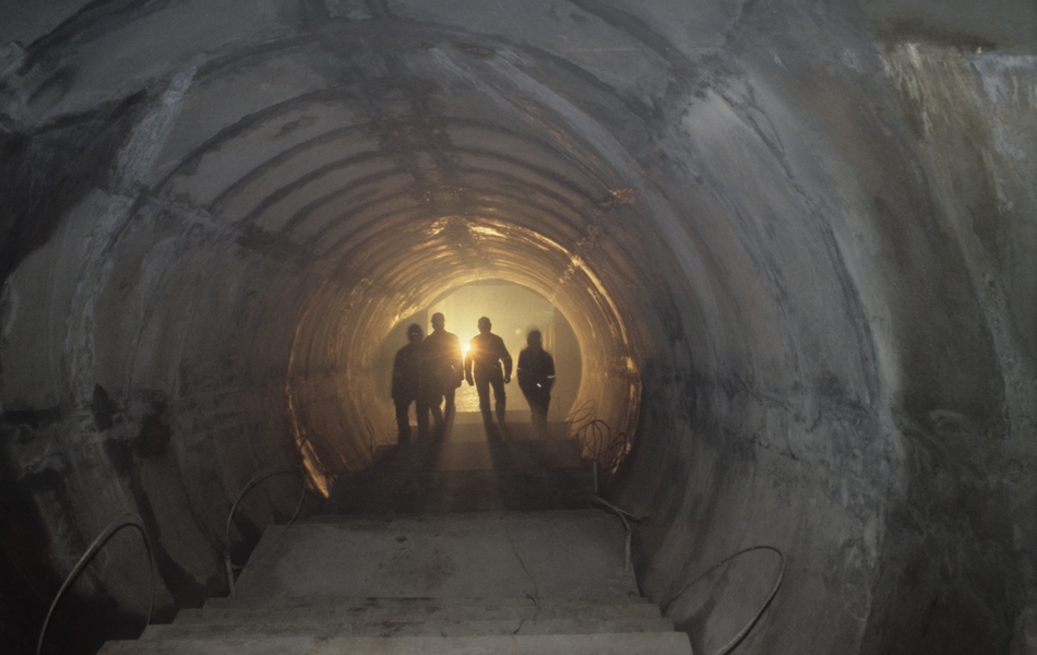 Photographie couleur montrant le bout d'un tunnel éclairé où l'on aperçoit la silhouette d'hommes.