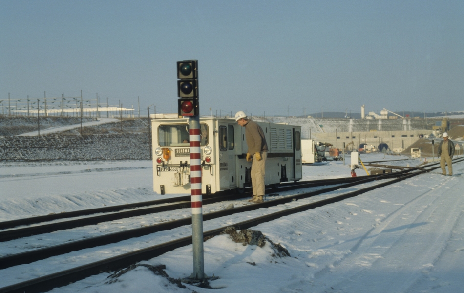 Photographie couleur montrant un chantier sous la neige. Au premier plan, on remarque un feu rouge, des rails et un wagonnet. 