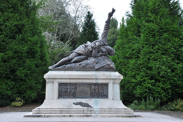 Photographie couleur montrant un monument représentant un soldat tombé et mortellement touché, le bras levé et tenant un pli.