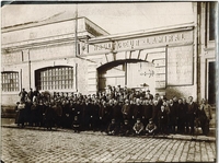 Photographie noir et blanc : le personnel de la société d'entreprises de construction et travaux publics d'Arras pose en groupe devant la façade de l'entreprise surmontée de l'inscription au fronton "Haultcoeur-Lamiral".