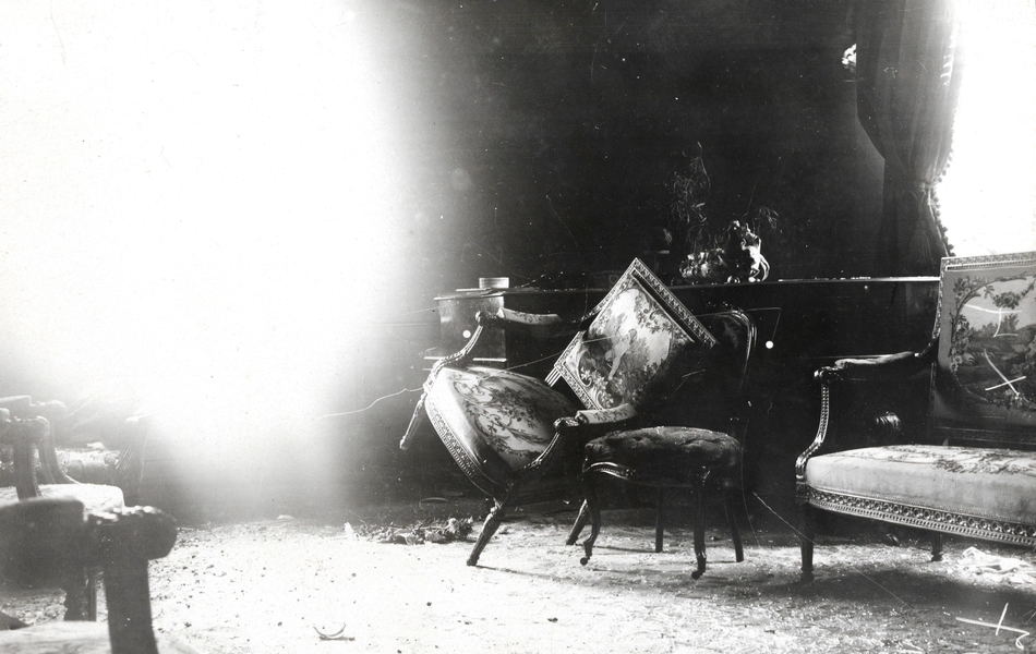 Photographie noir et blanc montrant un fauteuil renversé dans un salon dévasté.