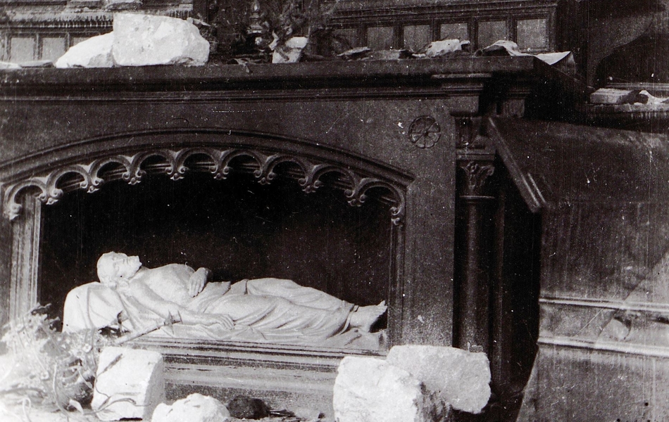 Photographie noir et blanc montrant une statue de gisant dans une église endommagée par des obus.