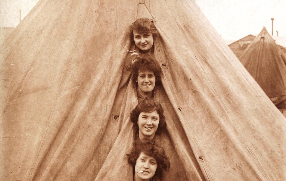 Photographie sepia montrant une tente dans l'ouverture de laquelle sortent quatre têtes de femmes.