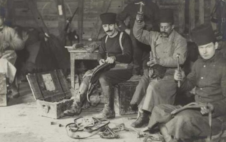 Photographie noir et blanc montrant des hommes assis, en train de travailler, le marteau à la main. 