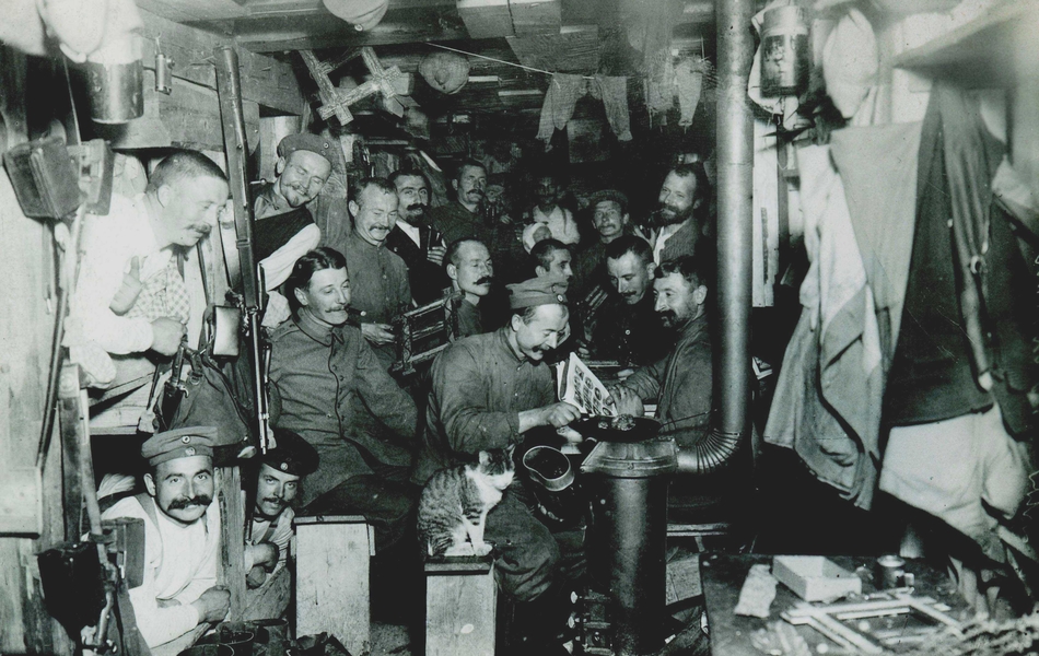 Photographie noir et blanc motrant une dizaine d'hommes entassés dans un abri de fortune. Au premier plan, l'un semble faire la lecture aux autres.