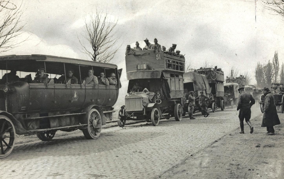 Photographie noir et blanc montrant des bus remplis de militaires qui se succèdent sur une route.