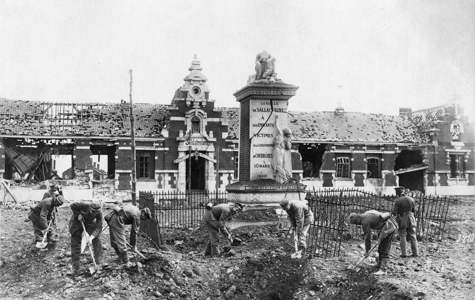 Photographie noir et blanc montrant un groupe de soldats en train de déblayer des gravas sur une place autour d'un monument.