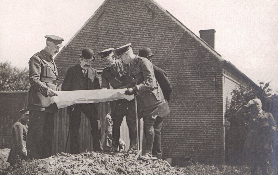 Photographie noir et blanc montrant deux civils et trois militaires sur un monticule, en train d'examiner un plan. 