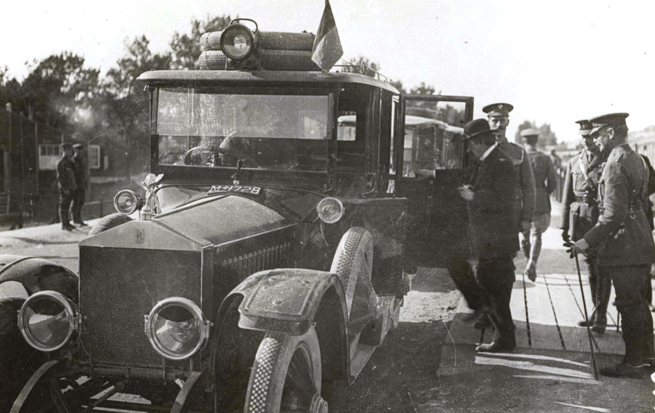 Photographie noir et blanc montrant un homme montant dans une voiture, entouré d'une délégation de militaires.