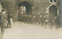 Carte postale noir et blanc représentant la troupe, à pied, passant sous l'une porte des fortifications de Boulogne-sur-Mer. 