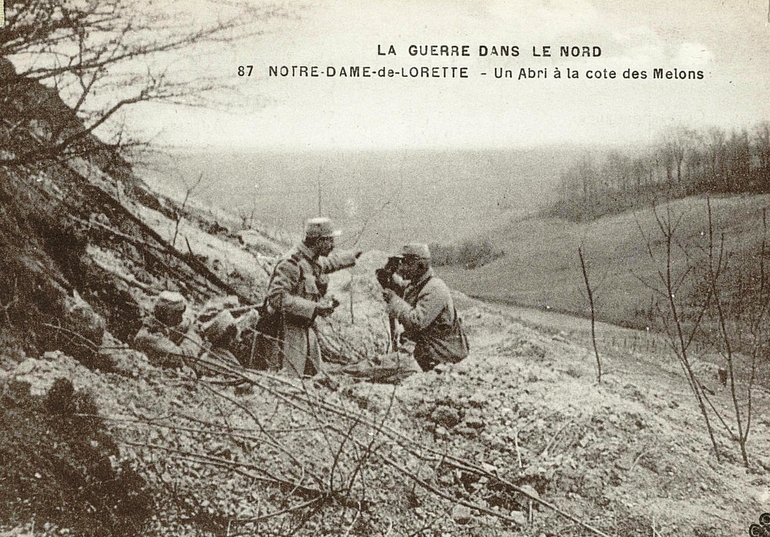 Carte postale noir et blanc montrant quatre hommes cachés dans une excavation sur le flanc d'une colline.