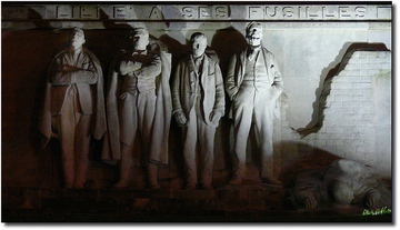 Photographie couleur montrant un monument commémoratif où l'on voit quatre hommes côte à côte tandis qu'un cinquième gît par terre. On lit au-dessus : "Lille a ses fusillés".