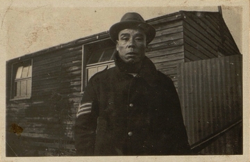 Photographie noir et blanc montrant un homme asiatique devant une cabane.