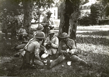 Photographie noir et blanc montrant des soldats en train de pique-niquer sous un arbre.
