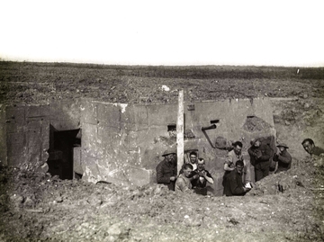 Photographie noir et blanc montrant un groupe d'hommes posant devant un blockaus à demi enterré.
