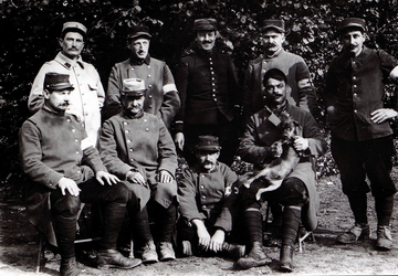 Photographie noir et blanc montrant un groupe de 9 soldats posant pour le photographe. L'un d'entre eux tient un chien sur ses genoux.