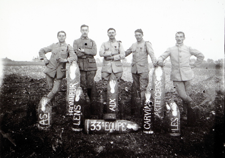 Portrait de cinq soldats disposés derrière des obus comportant les inscriptions suivantes : "AS. Honneur. Lens. Aux. 33e équipe. Carvin. Artificiers. Les".