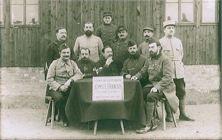 Photographie noir et blanc montrant un groupe d'une douzaine d'hommes en tenue militaire assemblés autour d'un écriteau (détaillé dans la légende).