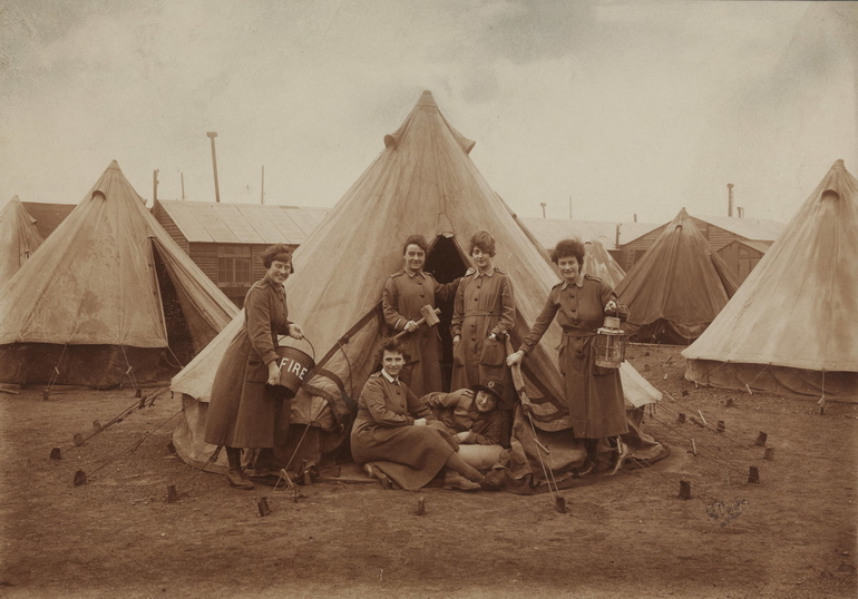 Photographie sépia montrant six femmes posant devant une tente.