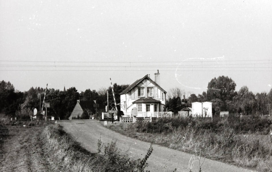 Photographie noir et blanc montrant une maison près d'un passage à niveau. 