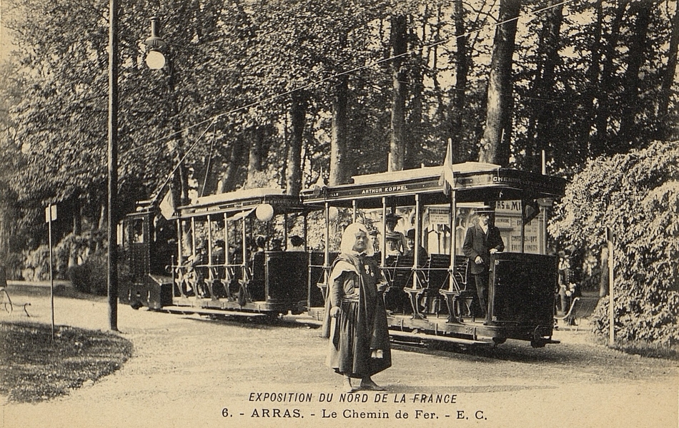 Carte postale noir et blanc d'un petit train roulant dans les allées du parc. Un homme habillé à la mode mauresque pose devant.