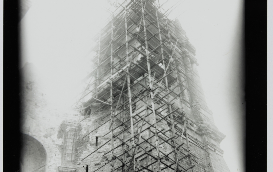 Photographie noir et blanc montrant les ruines de tours contre lesquelles on a monté un échafaudage.