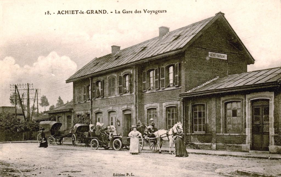 Carte postale noir et blanc montrant la gare devant laquelle posent les passagers de trois carrioles et d'une automobile