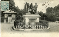 Carte postale noir et blanc d'un piédestal sur lequel reposent les statues de six personnes dans diverses postures. Au premier plan, de gauche à droite, un premier homme, légèrement voûté, la tête tournée, lève un bras. Le second, les bras le long du corps, regarde vers le sol. Le troisième, la tête haute, tient une grosse clé dans ses mains. Le monument se trouve dans un parc, devant un kiosque à journaux.