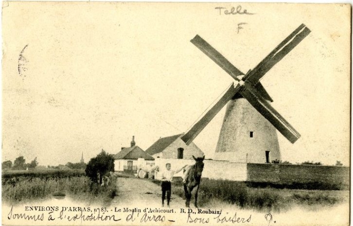 Photographie noir et blanc d'une ferme et d'un moulin dans la campagne. Au premier plan, un homme marche à côté d'un cheval.
