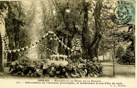Carte postale noir et blanc montrant une fontaine rocailleuse au premier blanc derrière laquelle s'étend une allée bordée d'arbres décorée de ballons.