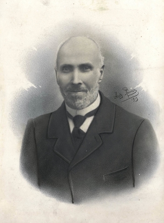 Photographie noire et blanc représentant le buste d'un homme en costume au collier de barbe blanc.