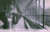 Carte postale noir et blanc montrant un couloir bordé de fenêtres et longé de patères auxquelles sont accrochés des manteaux.