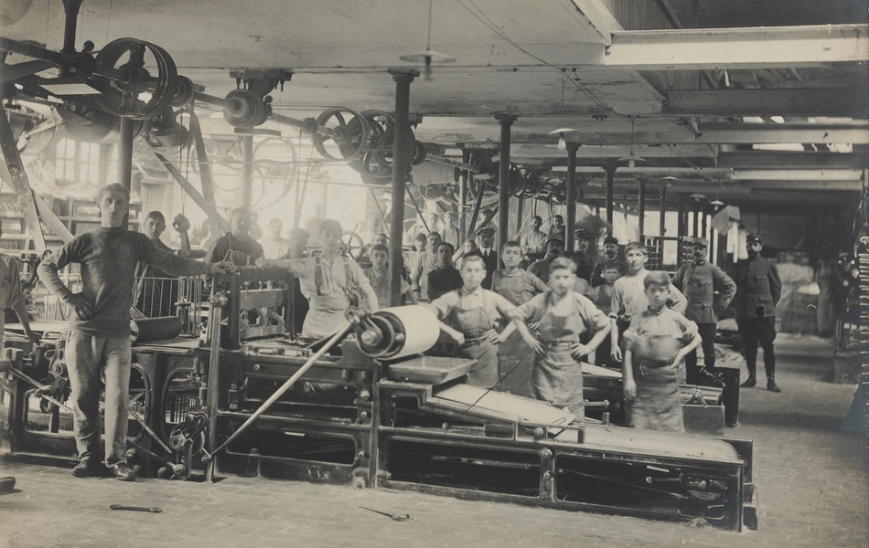 Photographie noir et blanc montrant de jeunes garçons entourés de machines dans une usine.