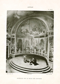 Illustration noir et blanc d'une scène ronde où se trouvent un piano droit, un pupitre à côté duquel est posé un étui et plus loin un violoncelle. Le décor représente une balustrade extérieure (on voit la végétation peinte en arrière-plan). Entre les colonnes se dressent des bustes sur des piédestaux. Enfin, le dôme peint des dieux et déesses antiques dans des nuages.