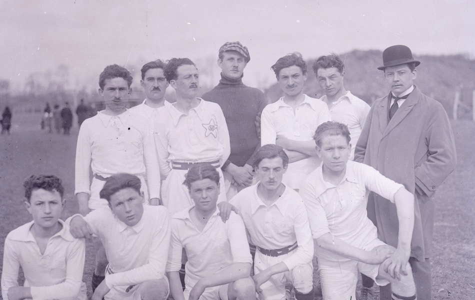 Photographie noir et blanc d'un groupe d'hommes posant en deux rangs. La plupart portent le même costume blanc (chemise et pantalon).