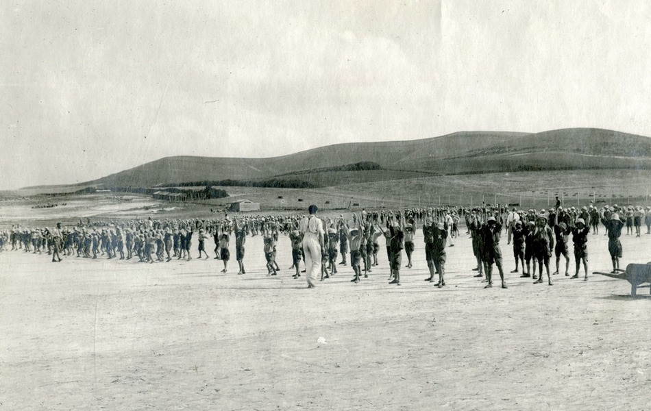 Photographie noir et blanc montrant une centaine d'écoliers faisant de la gymnastique sur une plage.