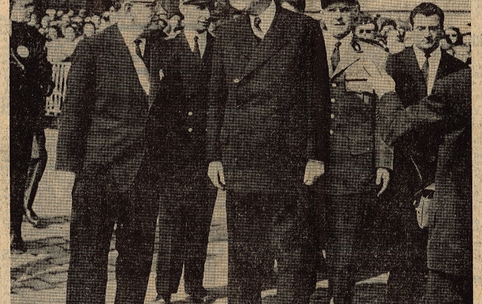 Photographie de presse sur laquelle on voit le général de Gaulle et le docteur Schaffner discutant face à face, entourés d’officiels. La foule est présente en arrière-plan derrière des barrières.