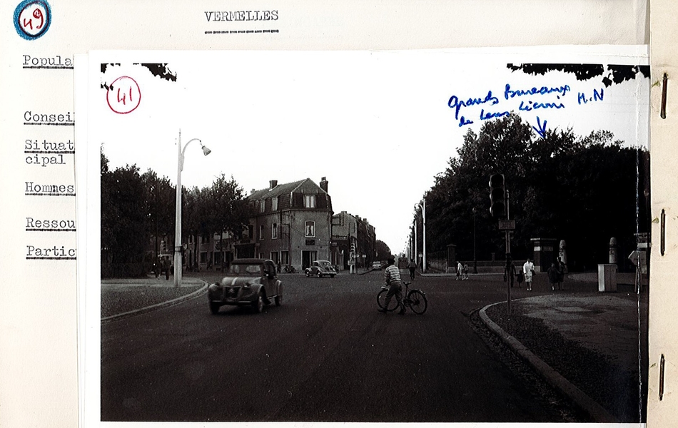 Photographie noir et blanc montrant un carrefour. Dessus, on lit : "Grands bureaux de Lens-Liévin. HN [Houillères nationales]".