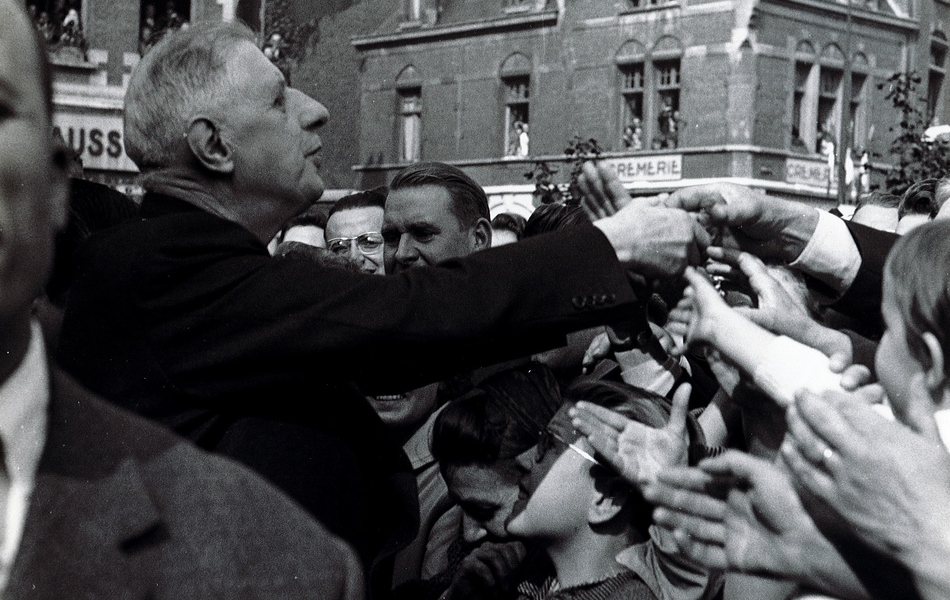 Photographie noir et blanc montrant un homme de profil serrant les mains de la foule.