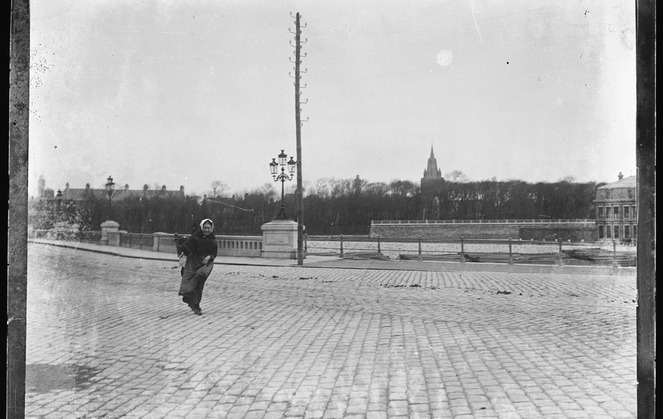 Photographie noir et blanc montrant une place pavée que traverse une femme.