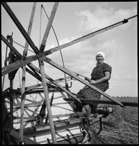 Photographie noir et blanc montrant une femme assise sur une machine agricole dans un champ.